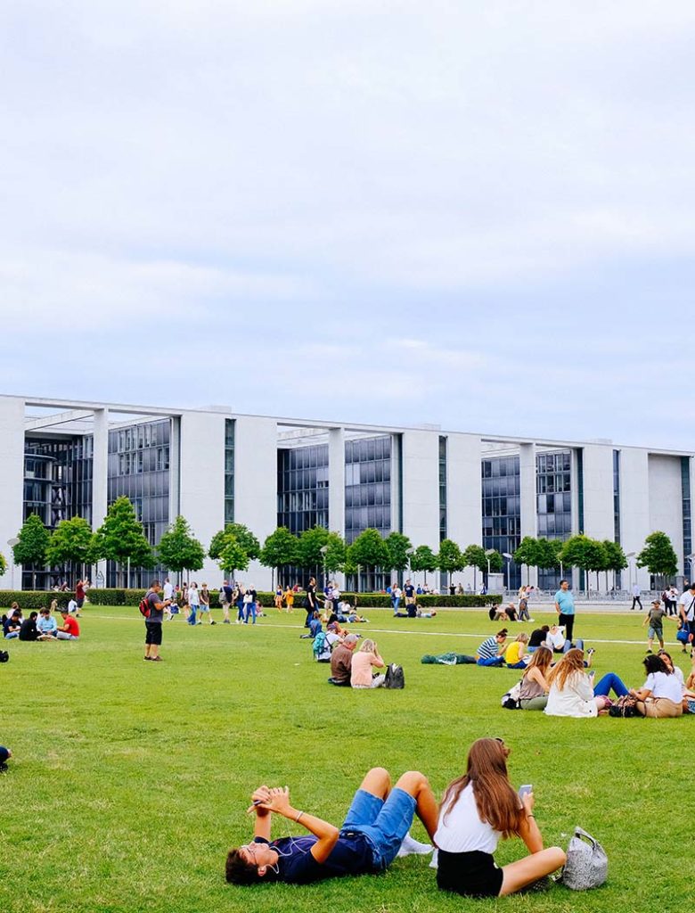 Students sitting on the green in front of buildings.