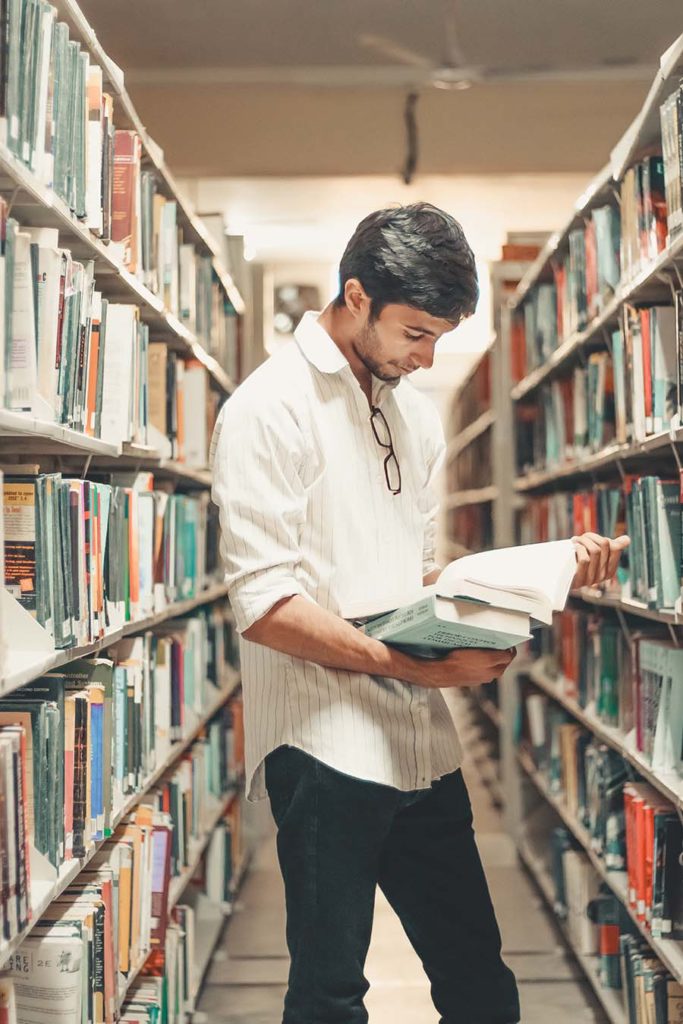 Male student standing between bookshelves in the library.