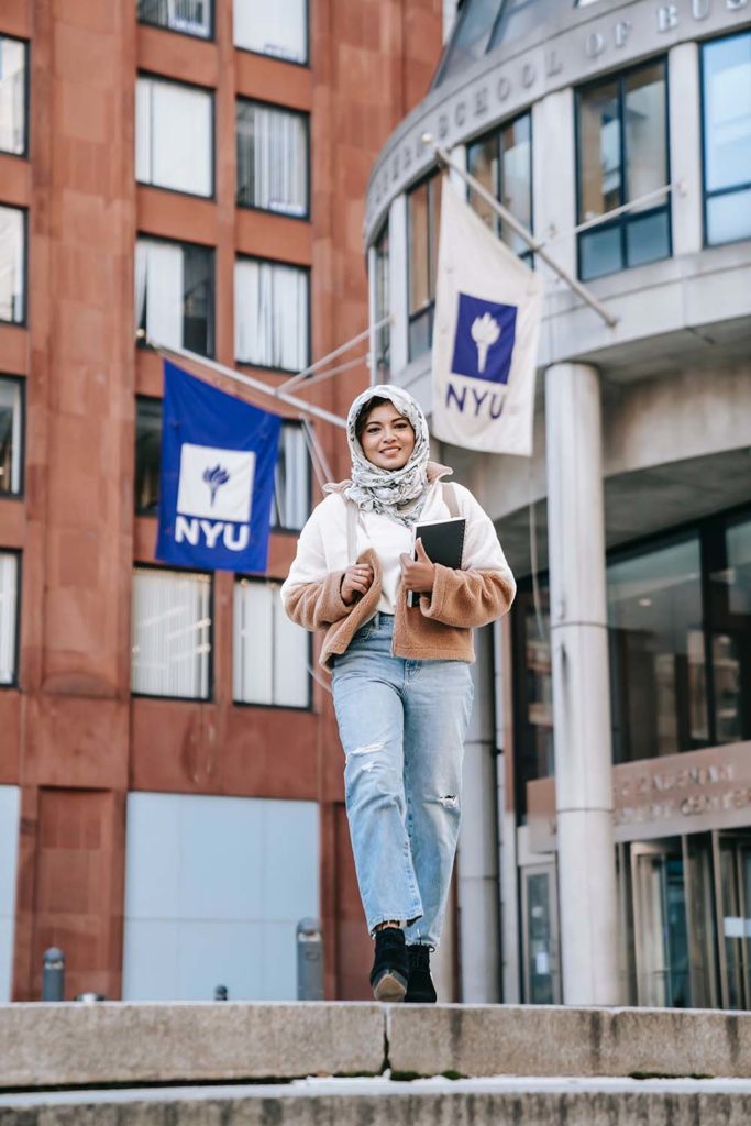Female student in hijab walking in front of NYU building. 