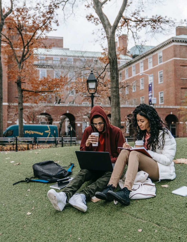 Two students sitting outside near campus studying. 