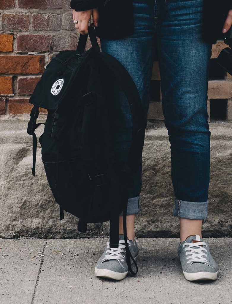 Student standing on sidewalk holding backpack. 